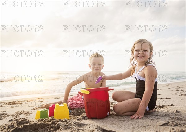 Boy (6-7) and girl (4-5) playing with sand on beach