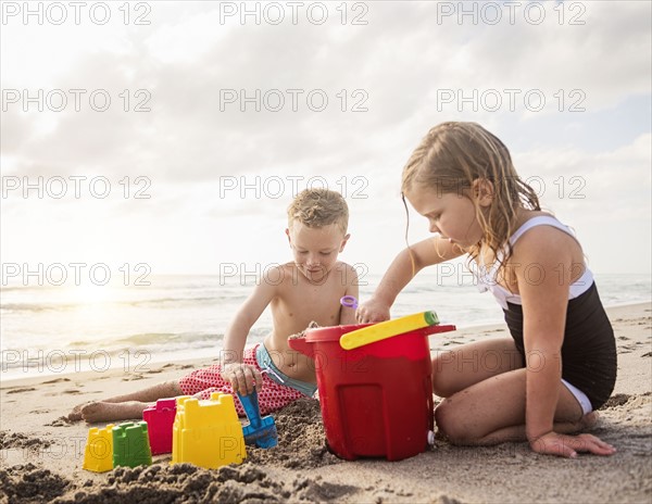 Boy (6-7) and girl (4-5) playing with sand on beach