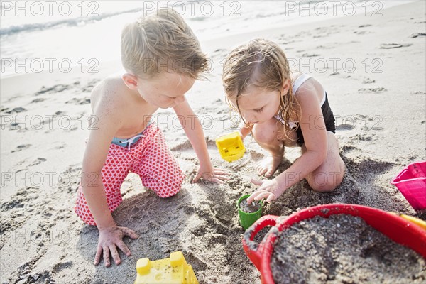 Boy (6-7) and girl (4-5) playing with sand on beach