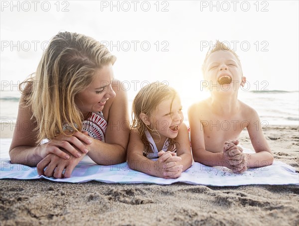 Mother lying down with son (6-7) and daughter (4-5) on beach