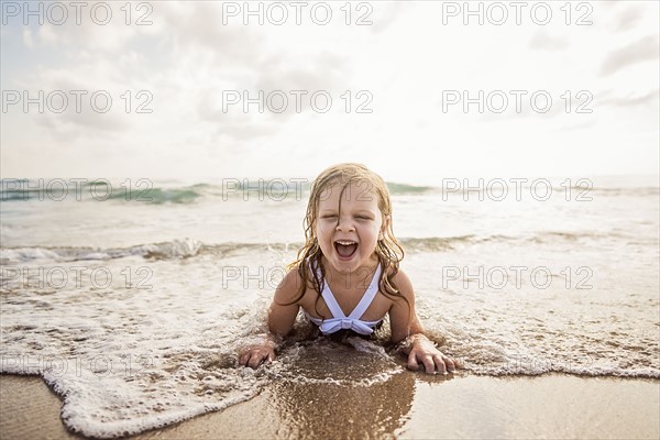 Girl (4-5) lying down in water on beach