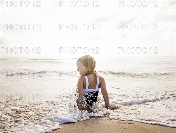 Girl (4-5) sitting in water on beach