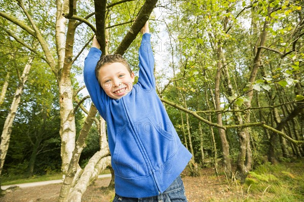 Smiling boy (6-7) hanging on tree
