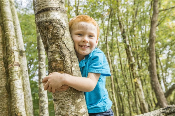 Smiling boy (2-3) hugging tree