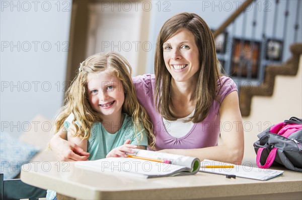 Smiling mother and daughter (8-9) sitting at table studying