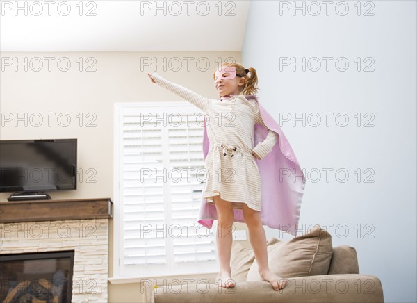 Little girl (4-5) playing superman on sofa