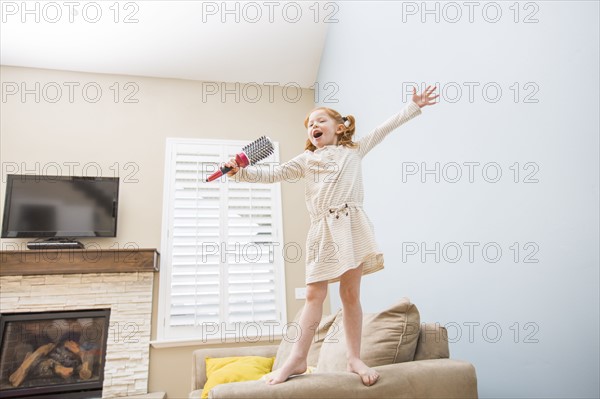 Little girl (4-5) singing into hairbrush on sofa