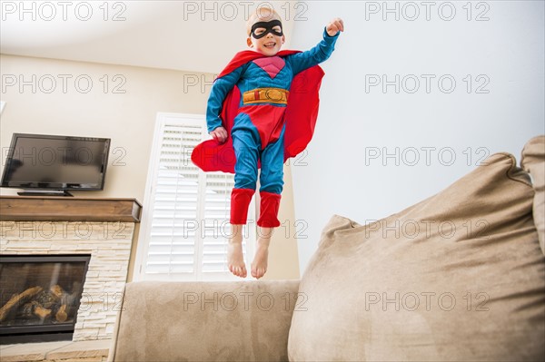 Little boy (2-3) in superman costume jumping on sofa