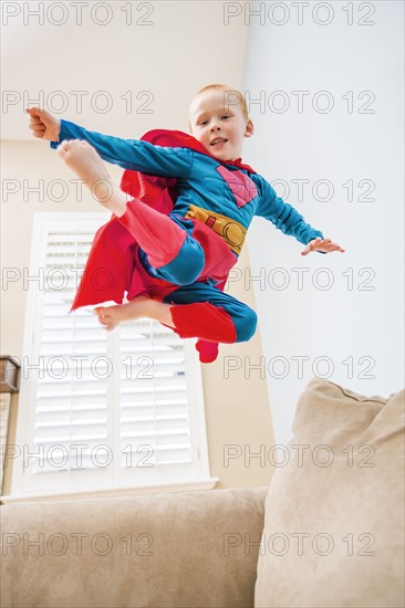 Little boy (2-3) in superman costume jumping on sofa