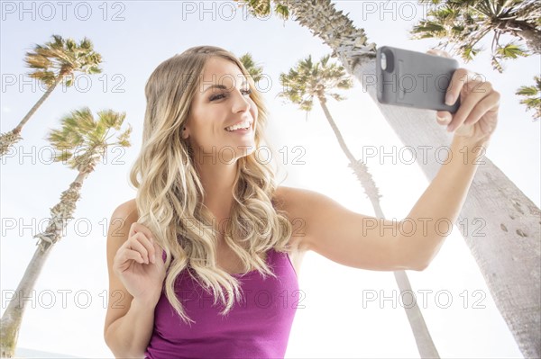 Smiling blonde woman taking selfie against palm trees