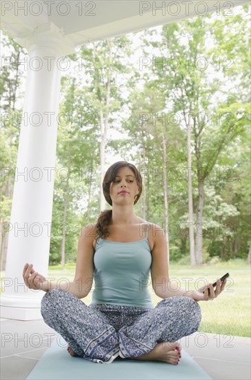 Young woman meditating and looking at smart phone