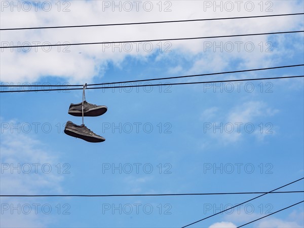Pair of shoes hanging on cable lines against sky