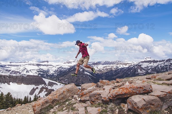 Mid adult man jumping over rocks in mountains