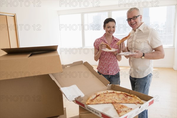 Portrait of smiling couple eating pizza in new apartment.