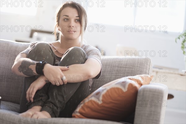 Sad woman sitting on sofa in living room.