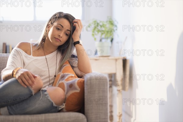 Sad young woman sitting on sofa.