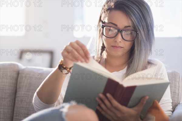 Young woman sitting on sofa and reading book.