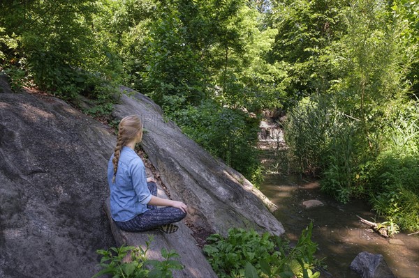 Woman sitting on stone in forest.