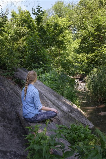 Woman sitting on stone in forest.