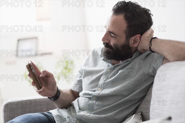 Mid-adult man using smartphone on couch.