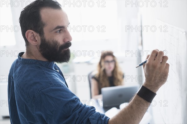 Mid-adult man writing on whiteboard.