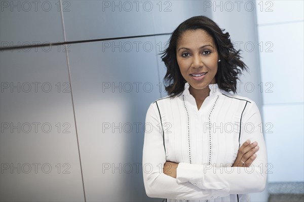 Portrait of woman with arms crossed against grey wall.