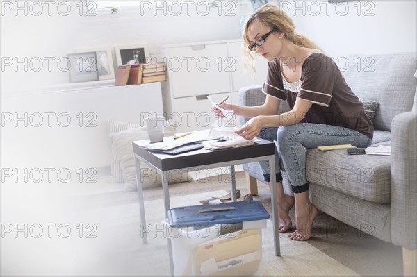 Woman sitting in living room and paying bills using electronic banking.