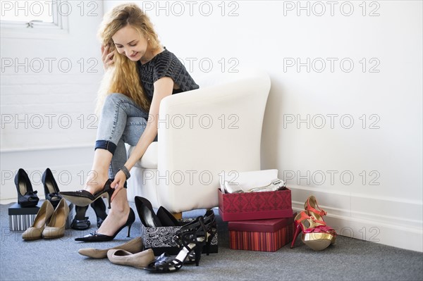 Woman trying on shoes sitting on white armchair.