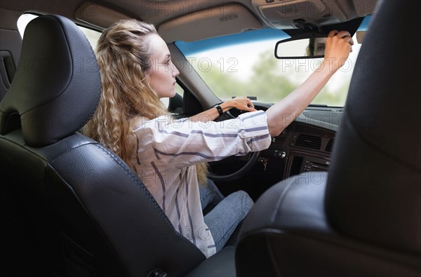 Woman adjusting rear-view mirror during driving car.