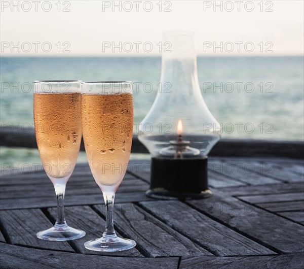 Wineglasses and oil lamp on table with sea in background