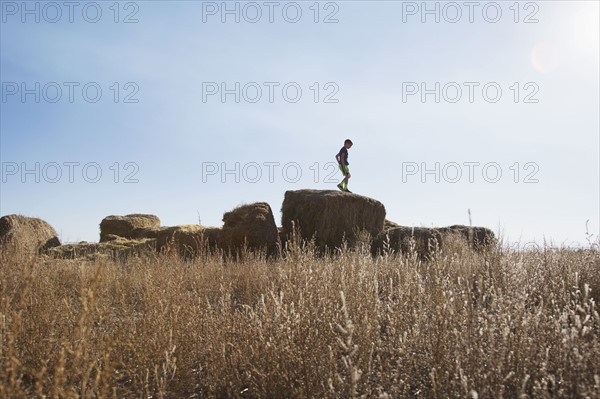 Boy (6-7) standing on bale of hay