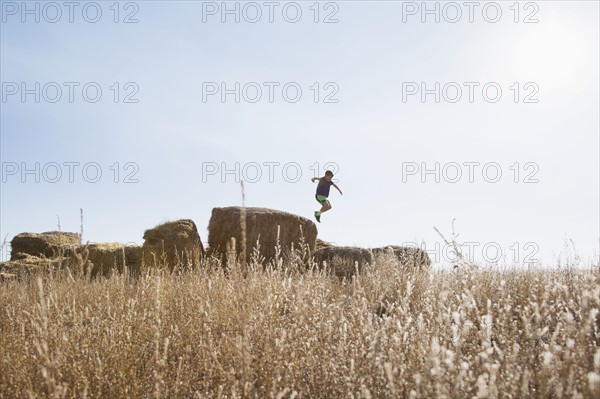 Boy (6-7) jumping on bale of hay