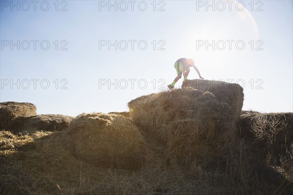 Boy (6-7) climbing on bale of hay