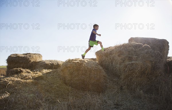 Boy (6-7) running on straw bales at sunset