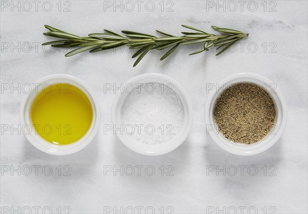 Overhead view of bowl of olive, salt, pepper and rosemary on marble table