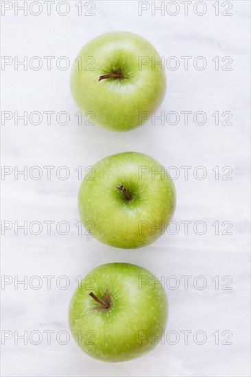 Overhead view of three apples on marble table