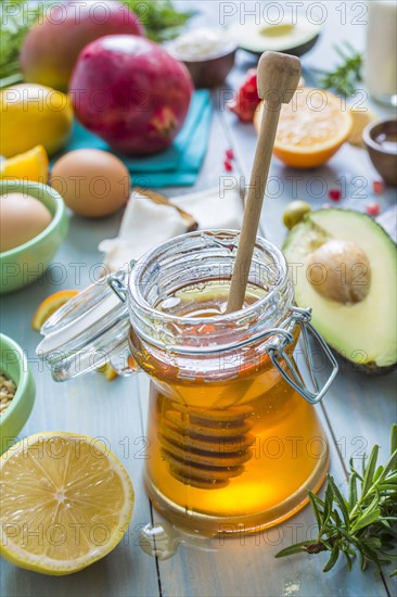 Jar of honey with dipper and fresh fruits and herbs