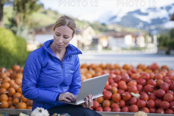 Austria, Salzburger Land, Maria Alm, Mature woman in blue jacket using laptop in market stall