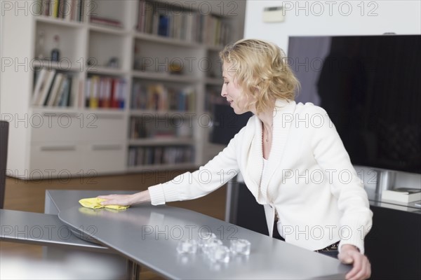 Mature woman cleaning table in living room