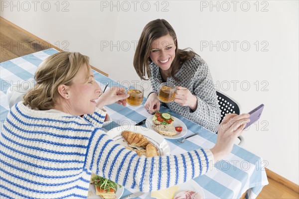 Women taking selfies with cups of tea at laid table in dining room