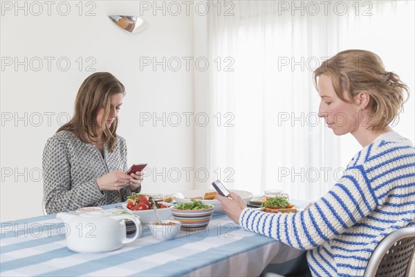 Women checking phones at laid table in dining room