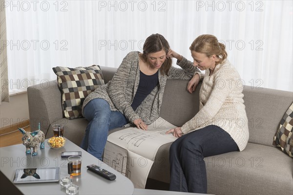 Women sitting on sofa and analyzing blueprint
