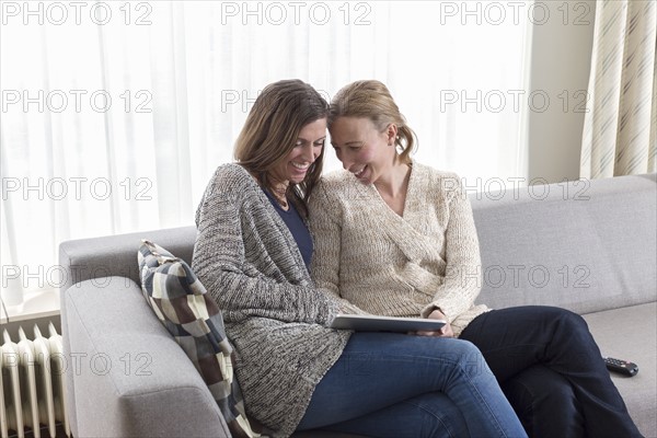 Women sitting on sofa and laughing looking at tablet