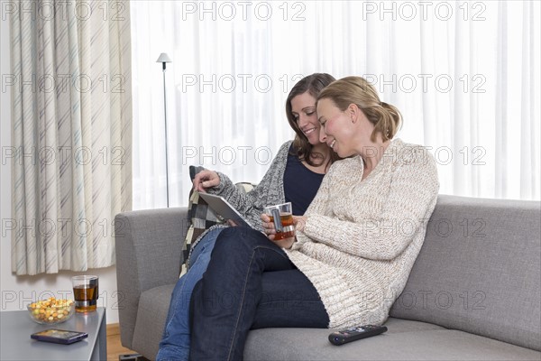 Women sitting on sofa and laughing looking at tablet