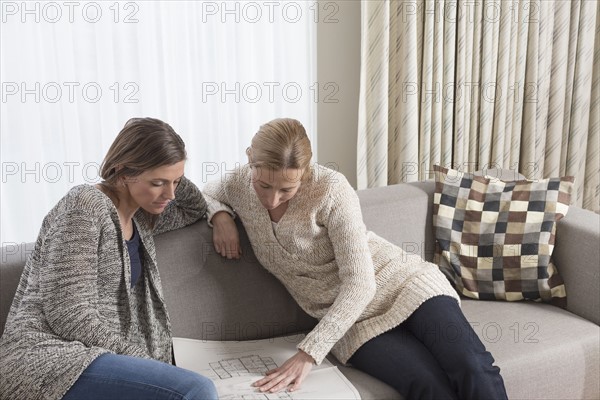 Women sitting on sofa and analyzing blueprint