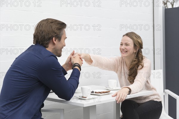 Man holding woman's hand as they seat at table with coffee