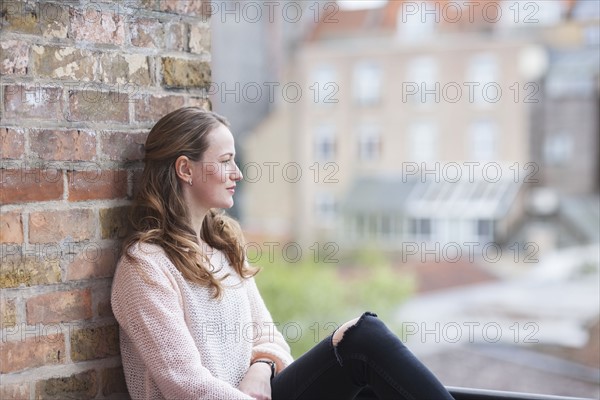 Mid-adult woman sitting and leaning against brick wall