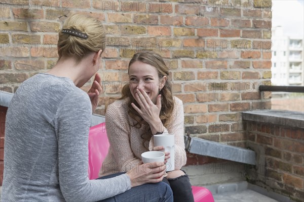 Women gossiping while sitting on balcony with coffee cups