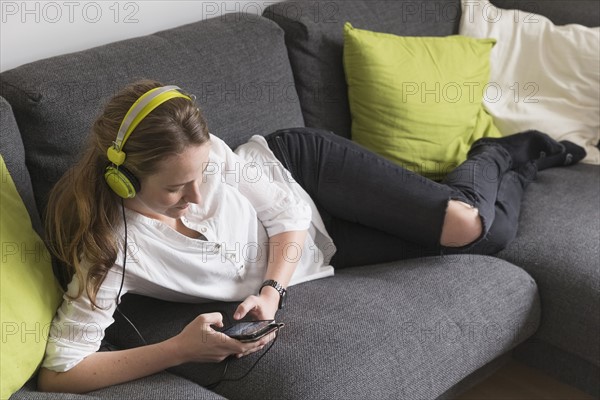 Mid-adult woman lying on sofa and listening to music from smart phone