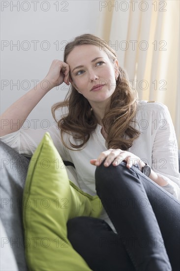Mid-adult woman sitting on sofa with legs curled up